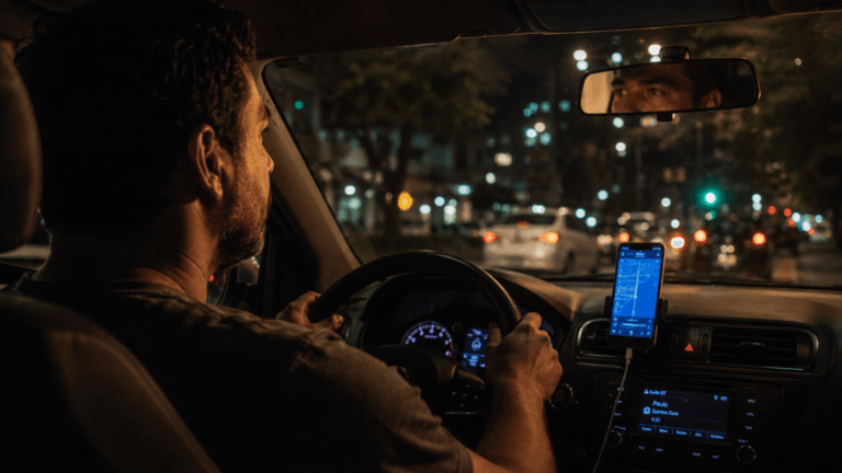 Motorista de app tem direito a carteira assinada? Motorista dentro do carro à noite verificando o celular