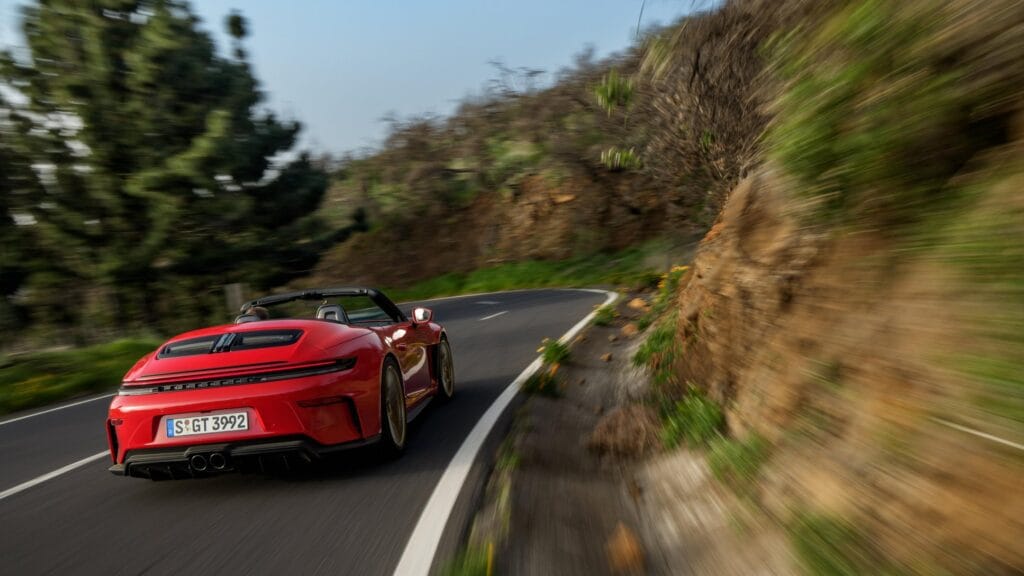Um Porsche 911 GT3 vermelho acelerando em uma curva sinuosa na montanha, representando a força, a velocidade e a emoção geradas por um powertrain a combustão de alta performance.